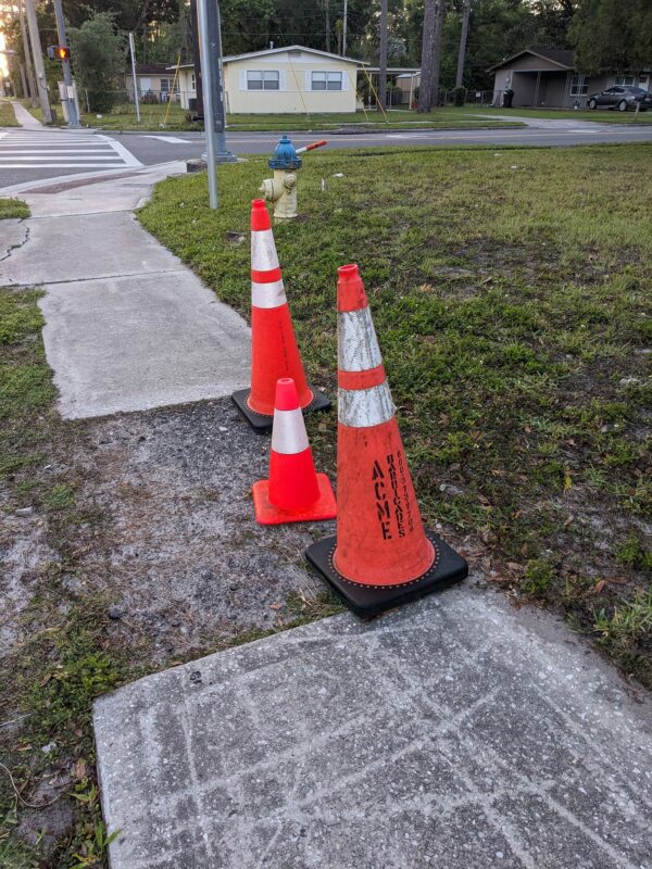 two large and one small traffic cone sit on a sidewalk