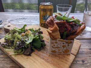 a small sandwich in a box next to a small salad on a cutting board