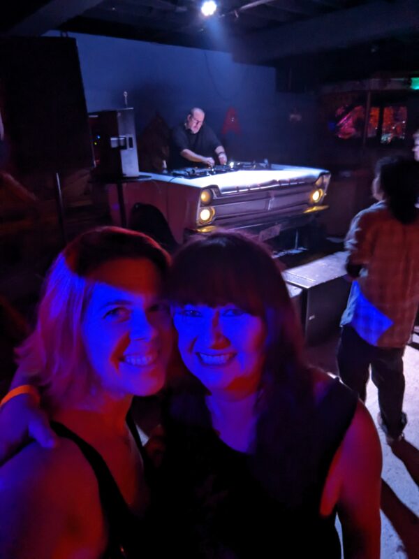 several people in the dramatic light and dark of a dance club with a dj in the background