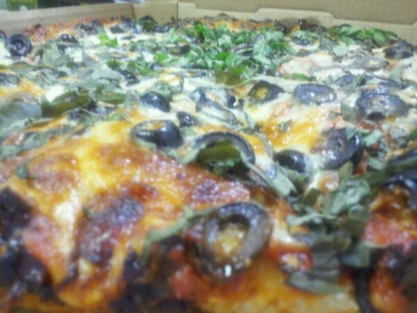 close up of a pizza with crusty cheese, black olives and basil