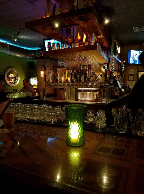 a bar with lots of bottles and glassware is lit by golden and green lights