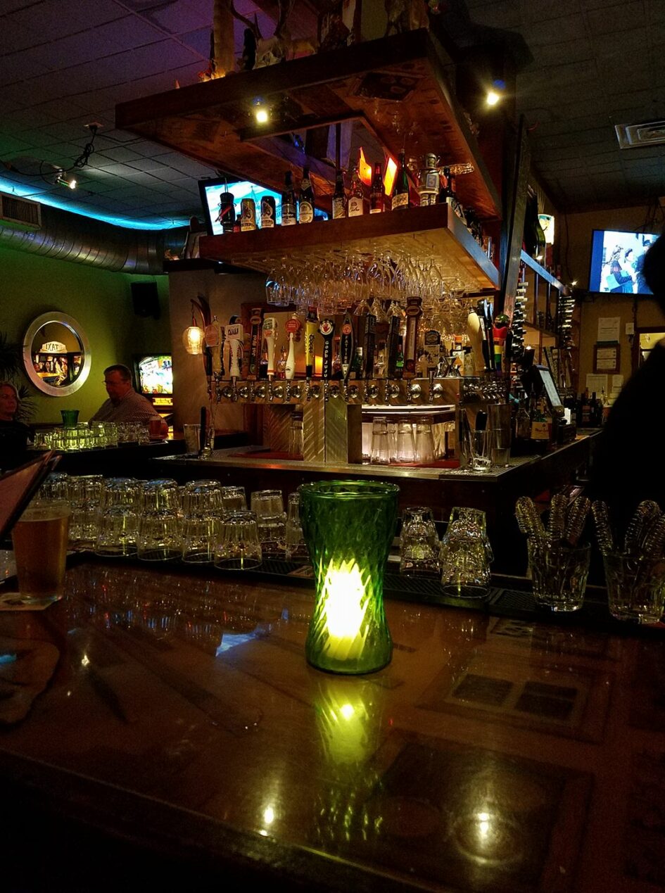 a bar with lots of bottles and glassware is lit by golden and green lights