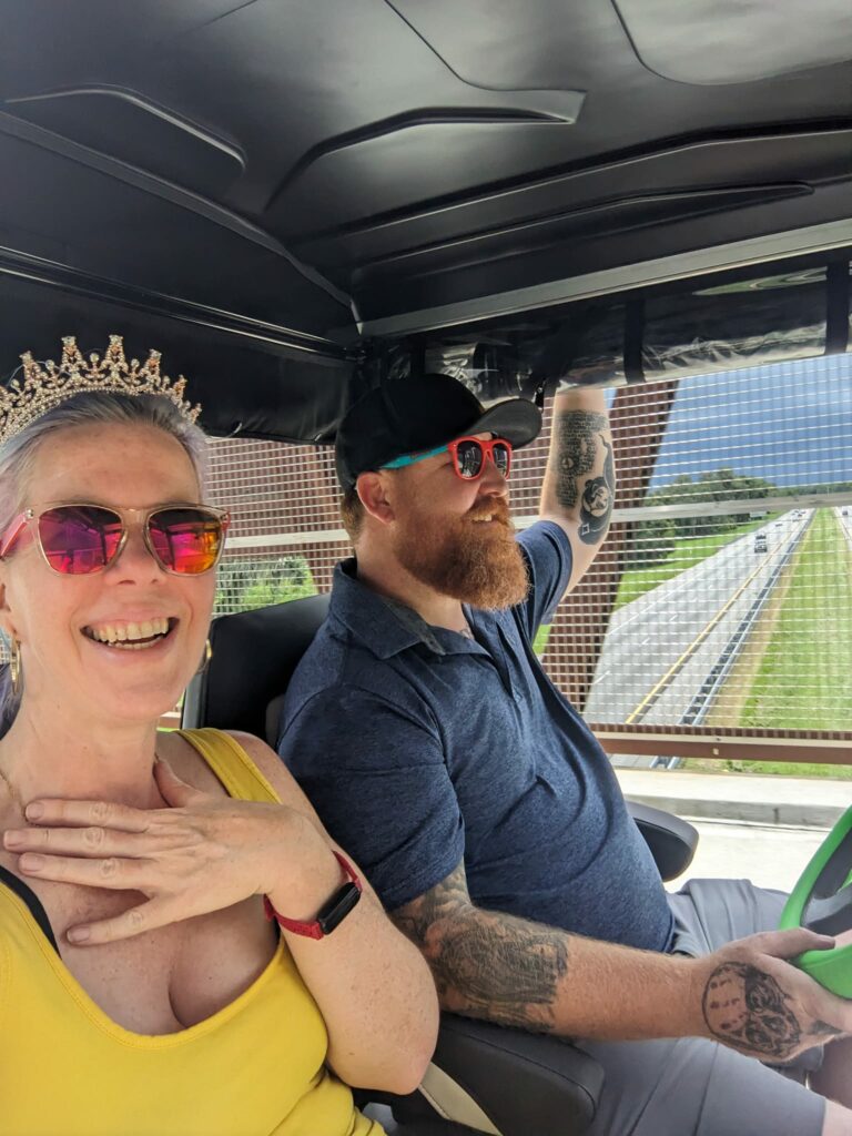 selfie in a tiara with a person driving a golf cart over a bridge