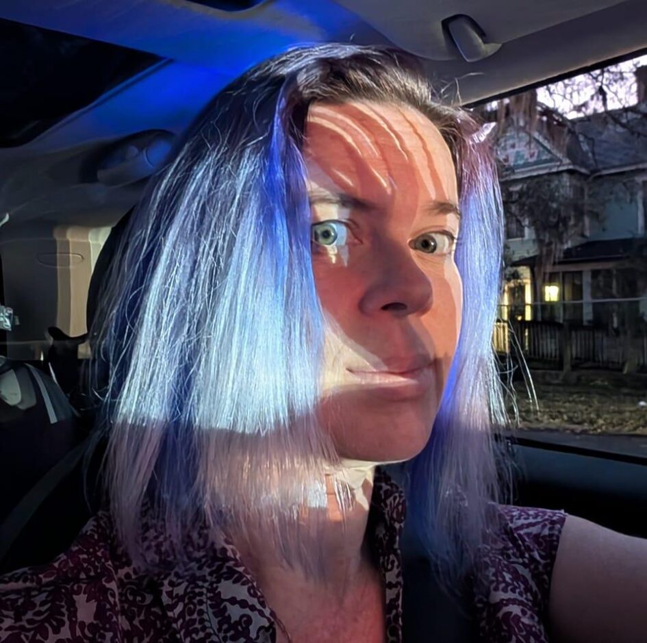 selfie of a person with dramatic lighting and blue hair that might have a spotlight on their face