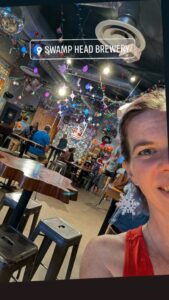 partial selfie of someone showing a public space like a bar or restaurant with strings of lights overhead in a fun but chaotic style