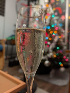 a champagne glass with a christmas tree out of focus in the background