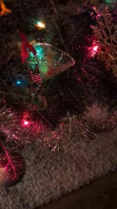 close up of a dark Christmas tree with lights and glitter shimmering and what looks like a small martini glass ornament