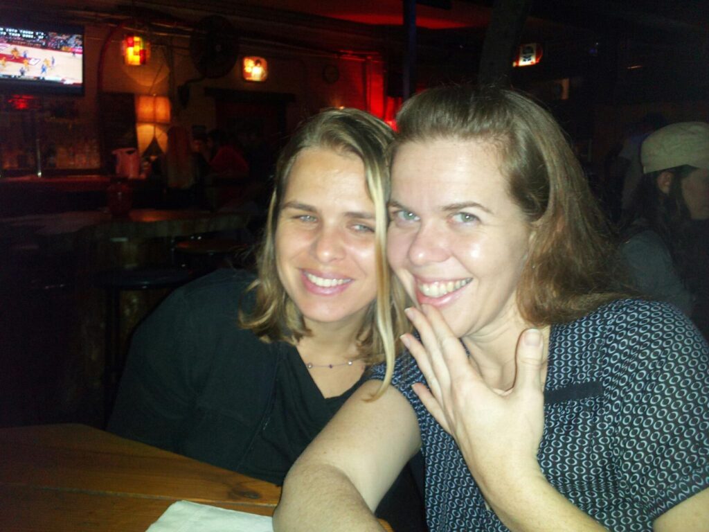 two people smiling into the camera in a bar of some kind