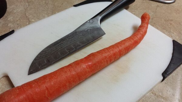 a large carrot with a strange bend at the end is sitting on a cutting board next to a big knife