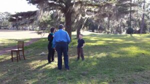 two adults and a child are talking near a tree covered in spanish moss