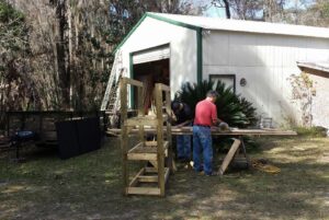 two people are using tools outside a warehouse to build a tower out of wood