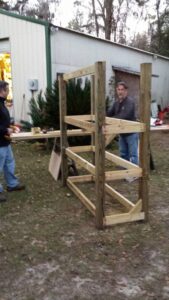 two people are building a rectangular wood tower out of lumber