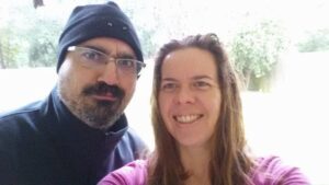 two people taking a selfie in very bright light, one wearing a knit cap and jacket