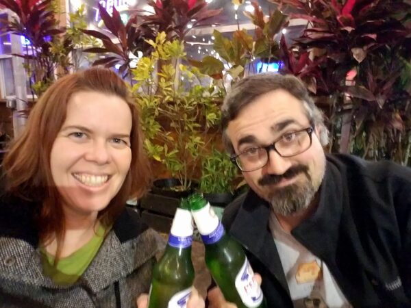selfie of two people in coats tapping two bottles of beer together as a toast