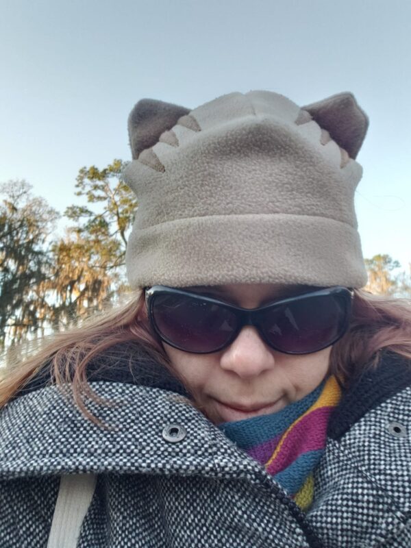 selfie of a person in a coat and sunglasses wearing a had with cat ears on it