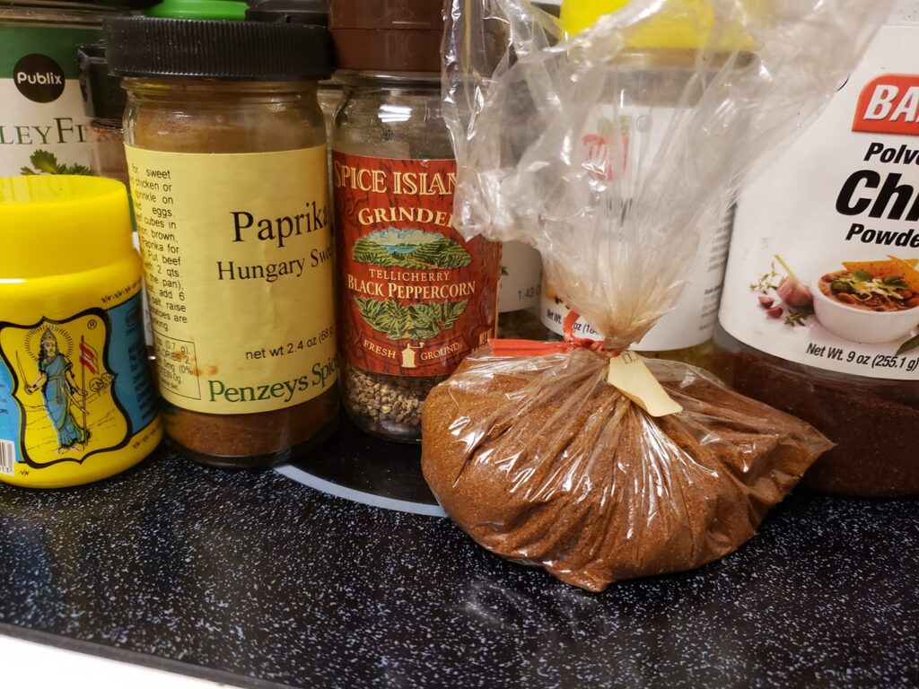 a row of bottle of spices and an unmarked bag of reddish spice