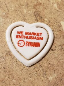 a heart shaped plastic thing has a logo and the word synanon imprinted into it