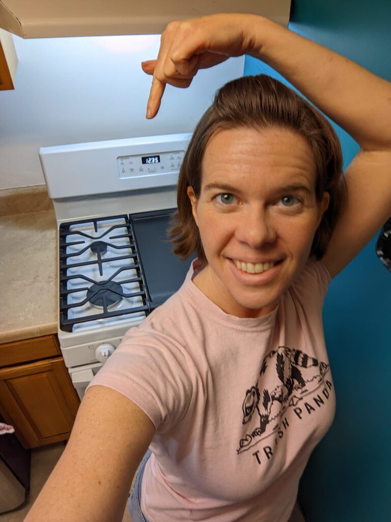 a person is pointing back over their shoulder at a stove in a kitchen