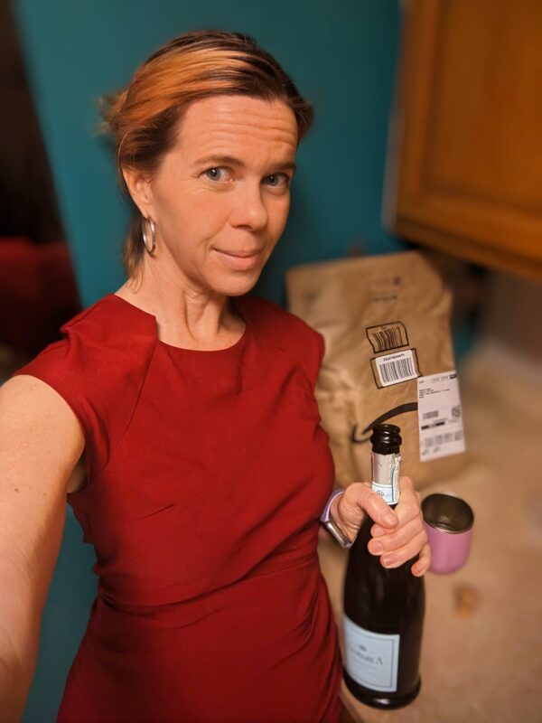 selfie of a person in a red dress holding what might be an open bottle of champagne