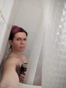 selfie of someone sitting in a shower holding a beer