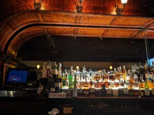 a wide wooden bar back has rows of bottles of liquor under dramatic lighting