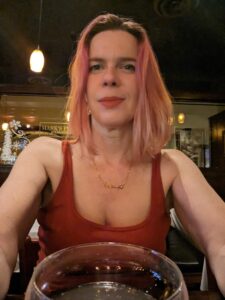 a selfie of a person in a red dress and lipstick over the rim of a cocktail glass in a bar