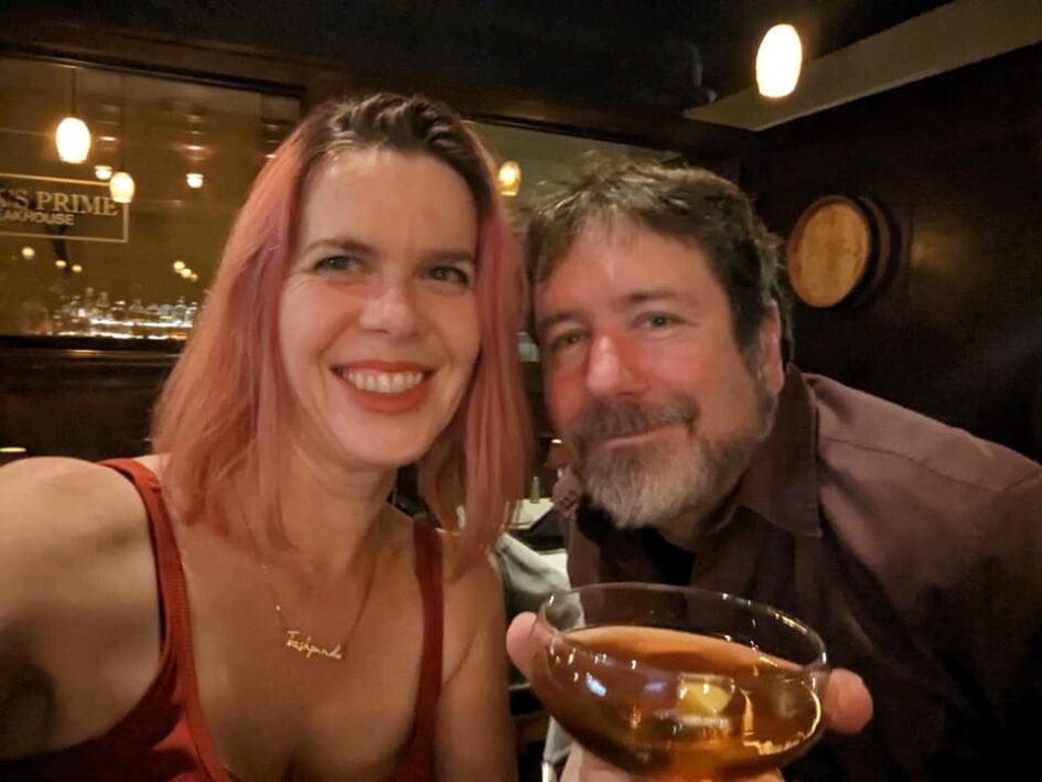 selfie of two people leaning towards each other in a bar with a cocktail in the foreground