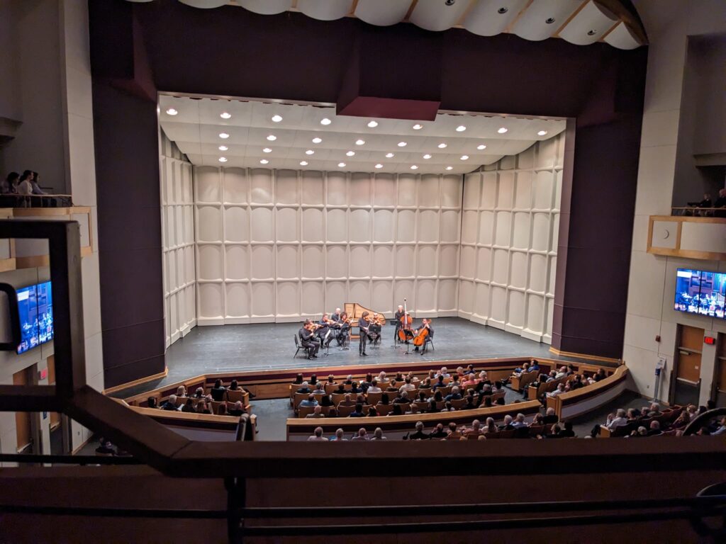 the large stage at a theater has a group o people playing stringed instruments like cello and violin