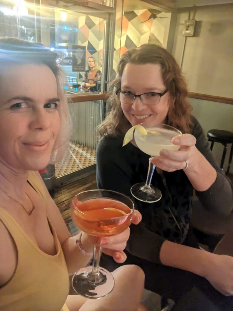 selfie of two women with red hair in a bar holding fancy cocktails