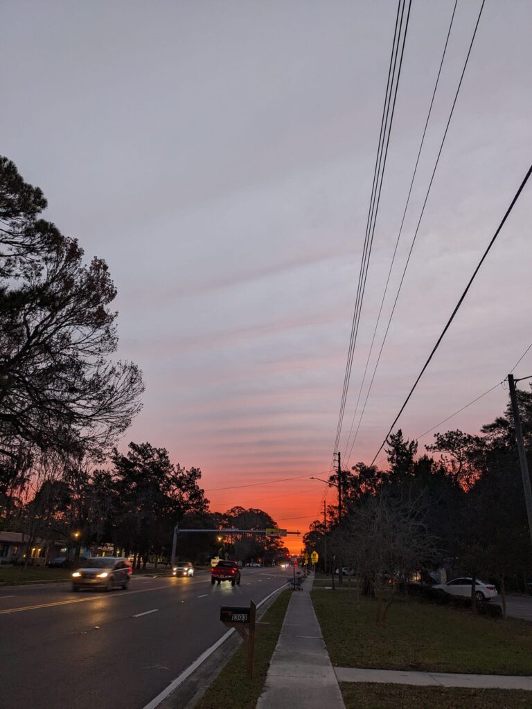 a sunrise on a neighborhood street with cars driving with headlights on