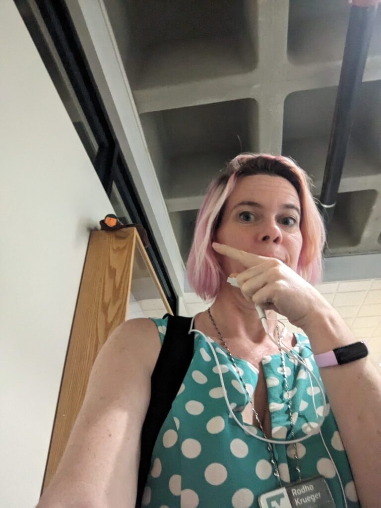a selfie of someone pointing over their shoulder to a plushy duck toy sitting at the top of a cabinet