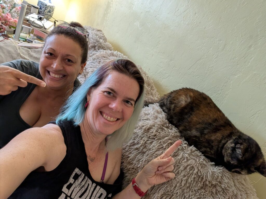 two people are pointing at a cat on the back of a couch