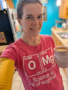 a person in a pink t-shirt with OMG Science is full of surprises on it and a cup of coffee