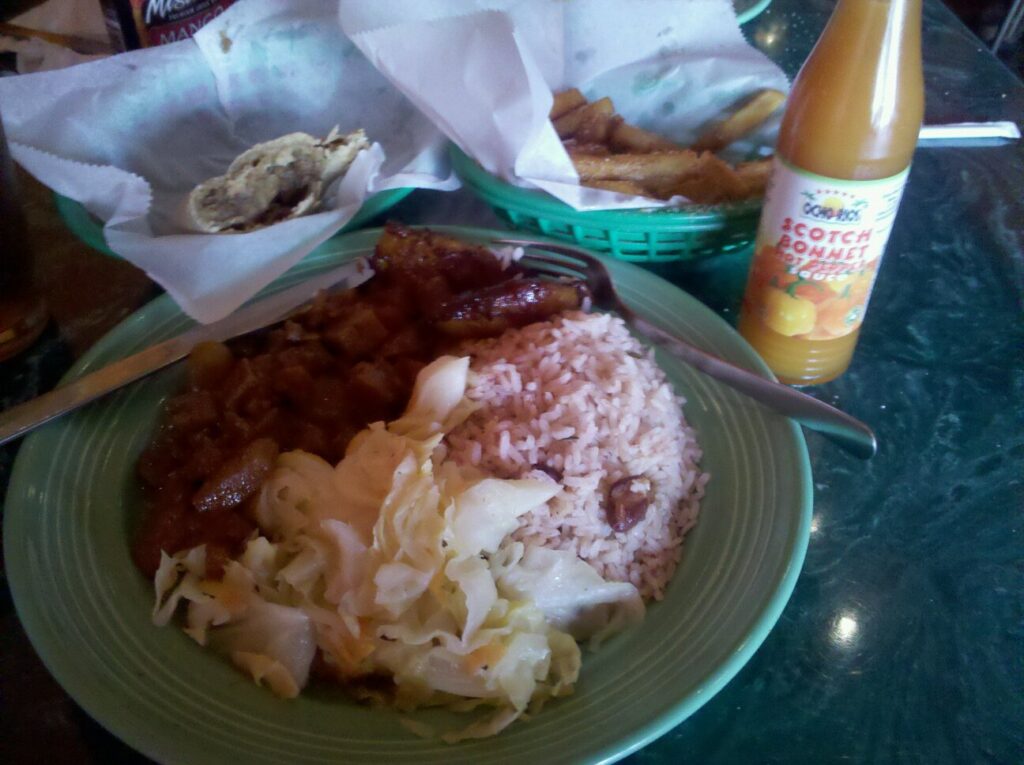 a plate of food at a restaurant of what looks like rice and cabbage and a bottle of hot sauce nearby