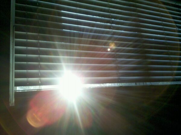 sharp sunlight is stabbing through a crack in some blinds