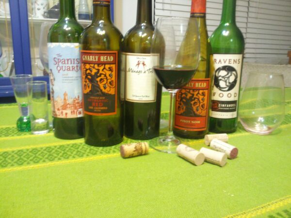 four empty wine bottles and several glasses are sitting on a grass green tablecloth