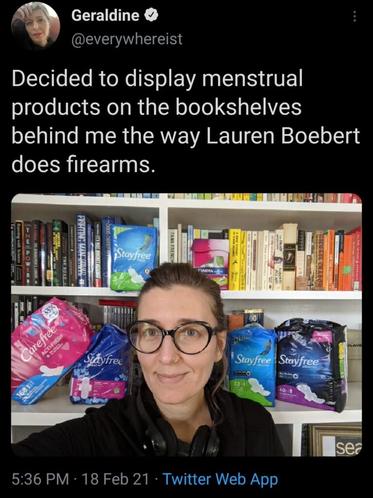 a picture of a woman with menstrual products behind her and the tweet saying Decided to display menstrual products o the bookshelves behind me the same way Lauren Boebert does firearms
