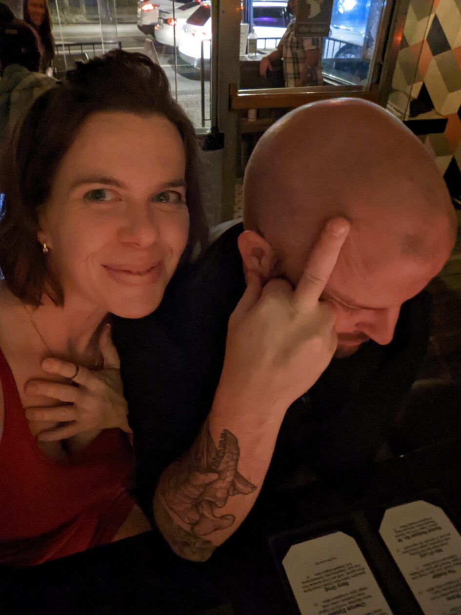 someone taking a selfie in a dak par while the person next to her casually holds up a middle finger