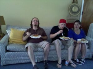 three people are sitting in a row on a couch balancing plates to eat