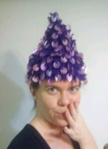 selfie of a person wearing a conical purple hat covered in purple coin-sized sequins
