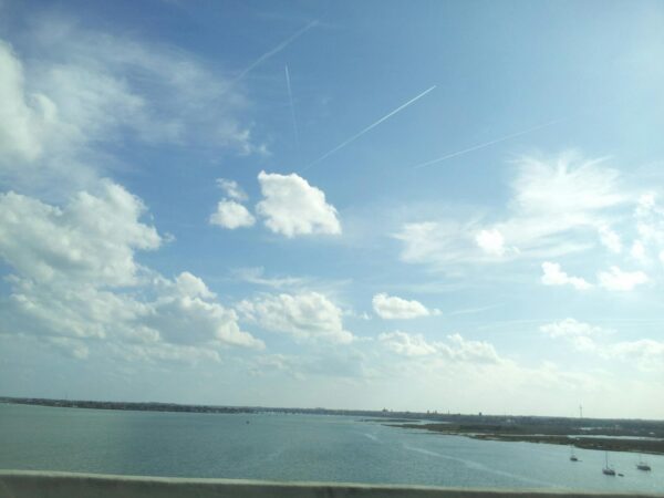a wide open sky with fluffy clouds dominates a flat body of water below