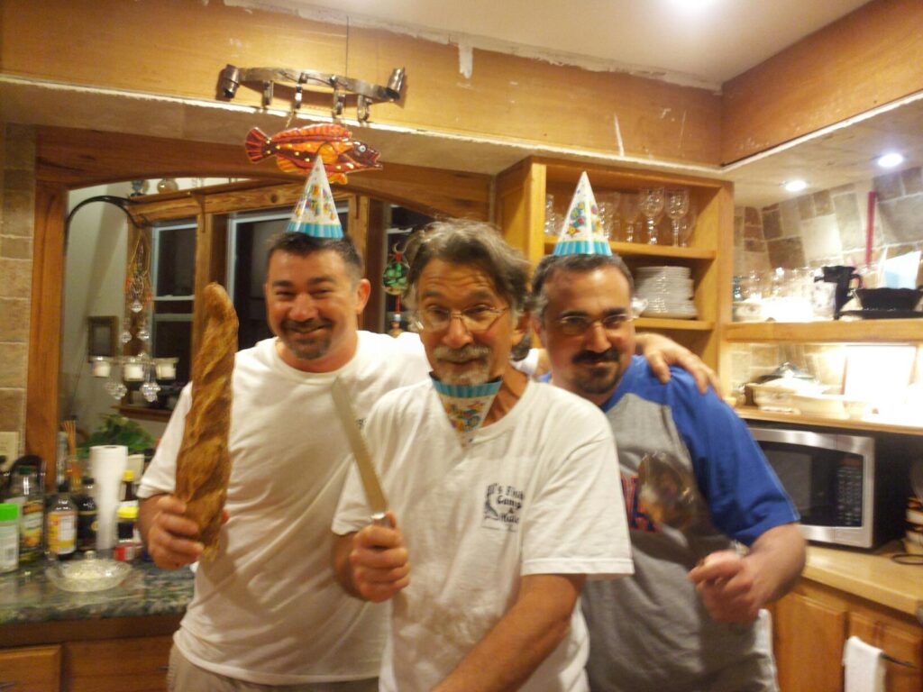 three people wearing birthday hats and holding baguettes like weapons in a kitchen