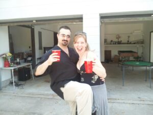two people holding red solo cups are laughing in a garage