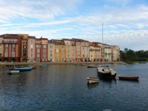 small empty boats are floating in a pond with a large hotel in the background made to look like an Italian sea village with many narrow townhouses in many colors