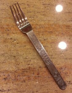 a fork with an odd pattern on its handle is laying on a rusty red marble countertop 