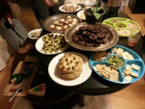 a table at a party is covered with trays and bowls of homemade looking snacks like cookies and dip and cheese and brownies