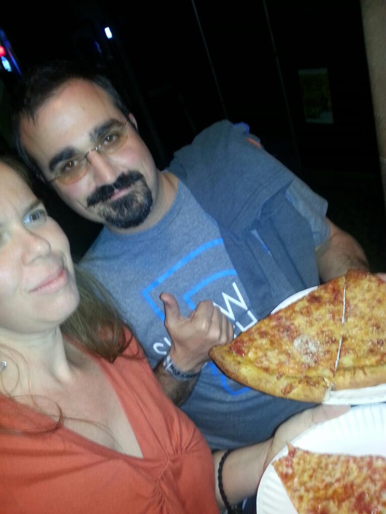 two people at night are holding large slices of pizza