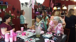 several people sit at a table and others are in a kitchen like a home party that could be a birthday or baby shower