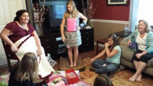several people are sitting around a living room as one person unwraps gifts