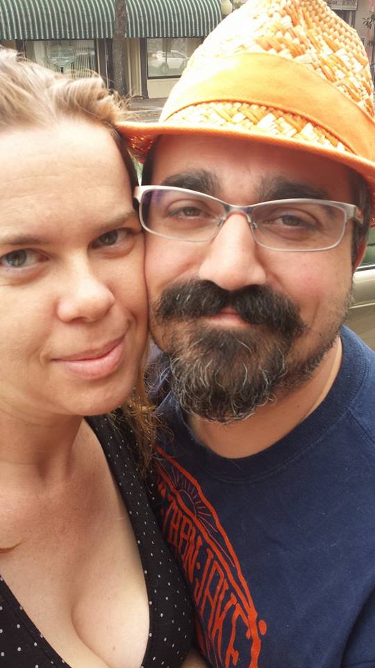 a selfie of two people, one looking unamused and the other wearing an orange woven hat